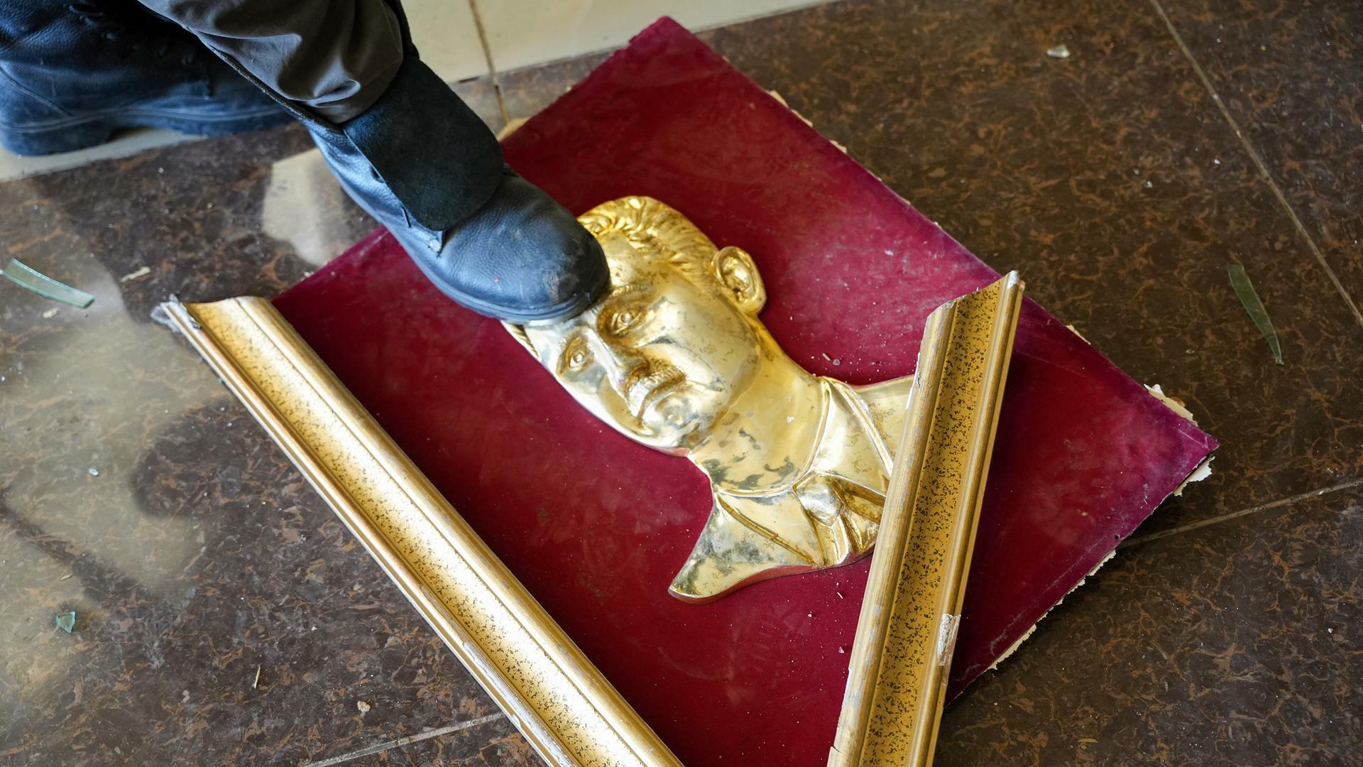 Ein regierungsfeindlicher Kämpfer steht in Aleppo auf einem zerbrochenen goldenen Porträt des syrischen Präsidenten Baschar al-Assad. 03.12.2024