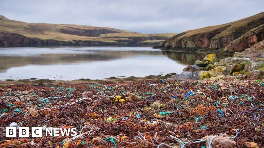 A calm loch surrounded by hills. In the foreground are lots of discarded fishing nets in a variety of colours