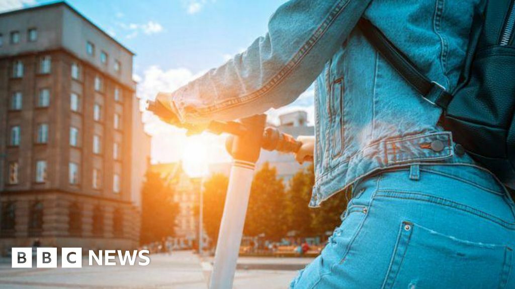 A person on an e-scooter riding in a town, with the sun setting in the background
