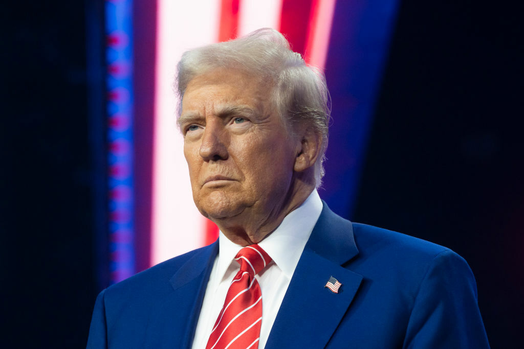 Donald Trump wears red, white and blue; he is frowning.