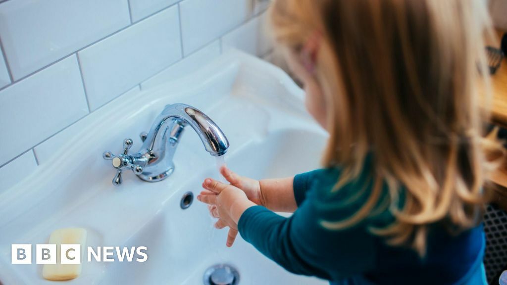 A young girl  with blonde hair washing her hands in the sink