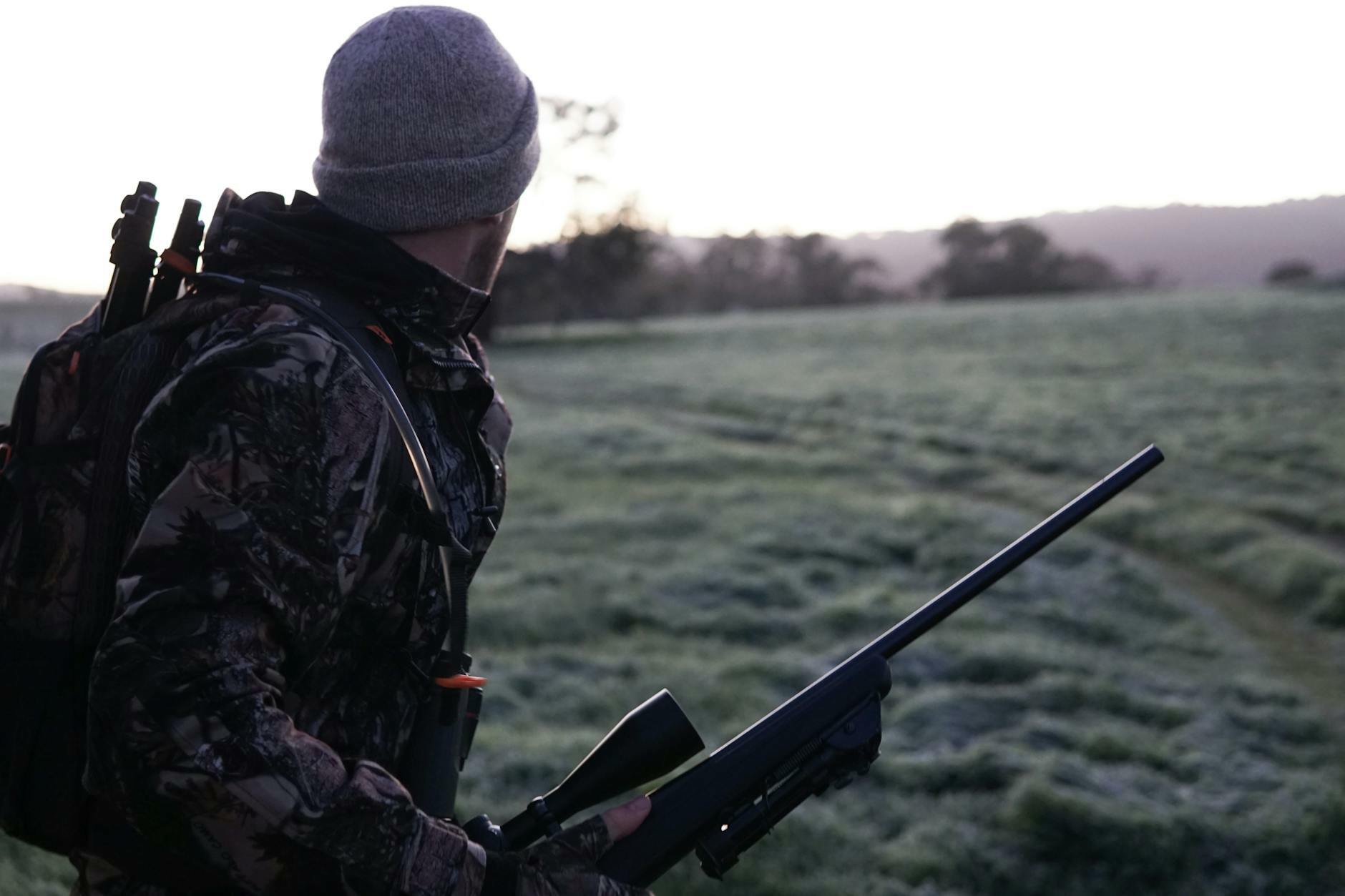 man wearing gray and black camouflage jacket holding rifle walking on grass field