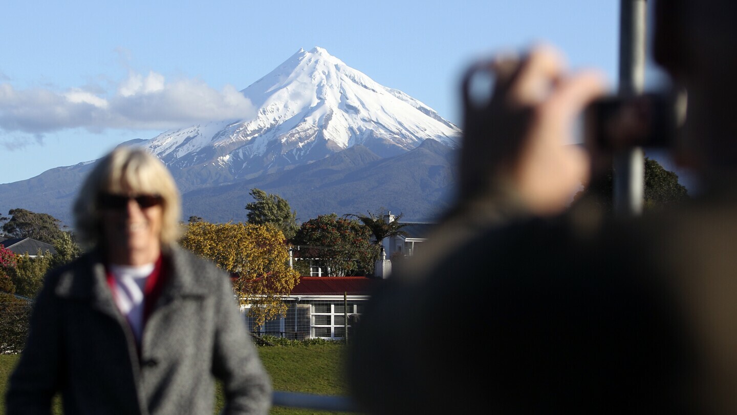 A man takes a picture of his wife with Mount Taranaki, also known as Mount Egmont, in the background in New Plymouth, New Zealand, Sept. 26, 2011. (AP Photo/Dita Alangkara, File)