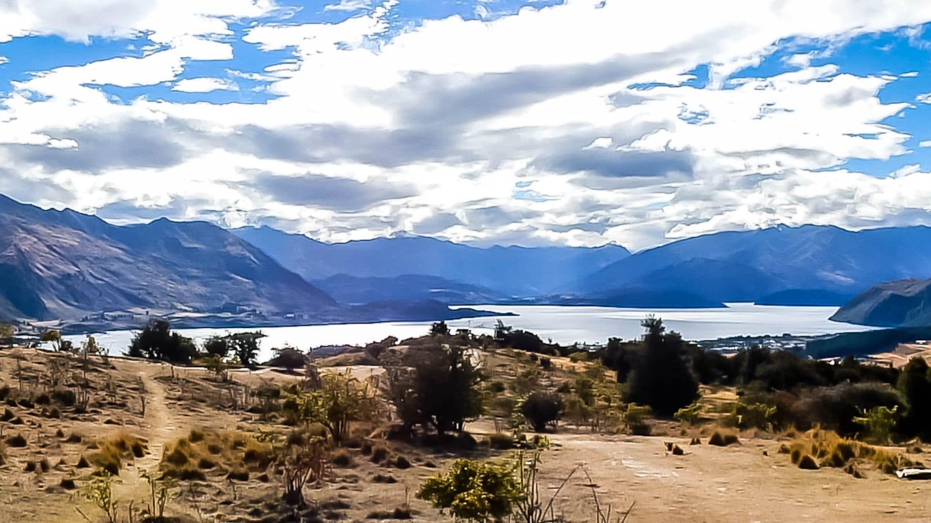 Uitzicht vanaf Mt Iron op een zonnige dag: blauwe lucht, witte wolken boven het meer en de bergen. Zanderige vlakte op de voorgrond.