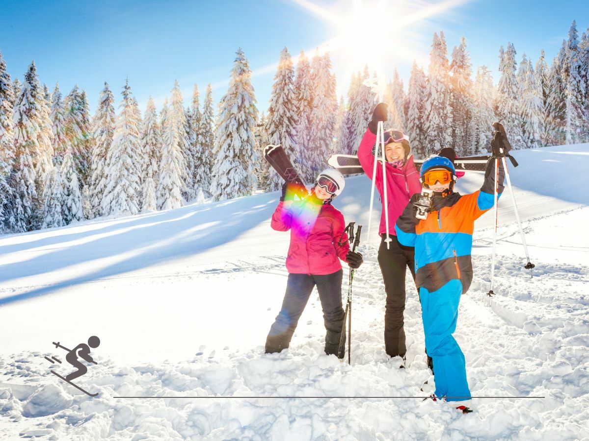 Three people in winter clothing standing on a snowy slope, holding ski poles and gear, with a forest and bright sun in the background.