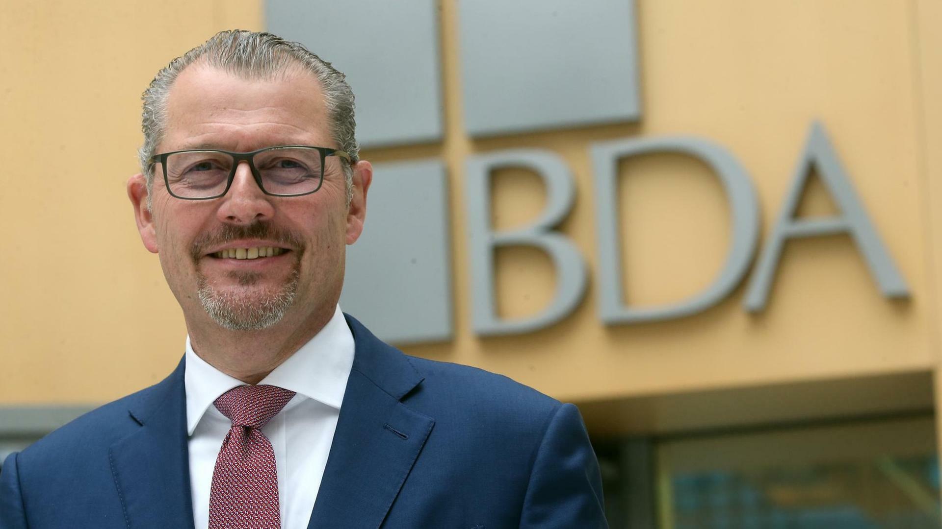 Rainer Dulge steht vor einem großen "BDA"-Logo, das an einer Wand angebracht ist.