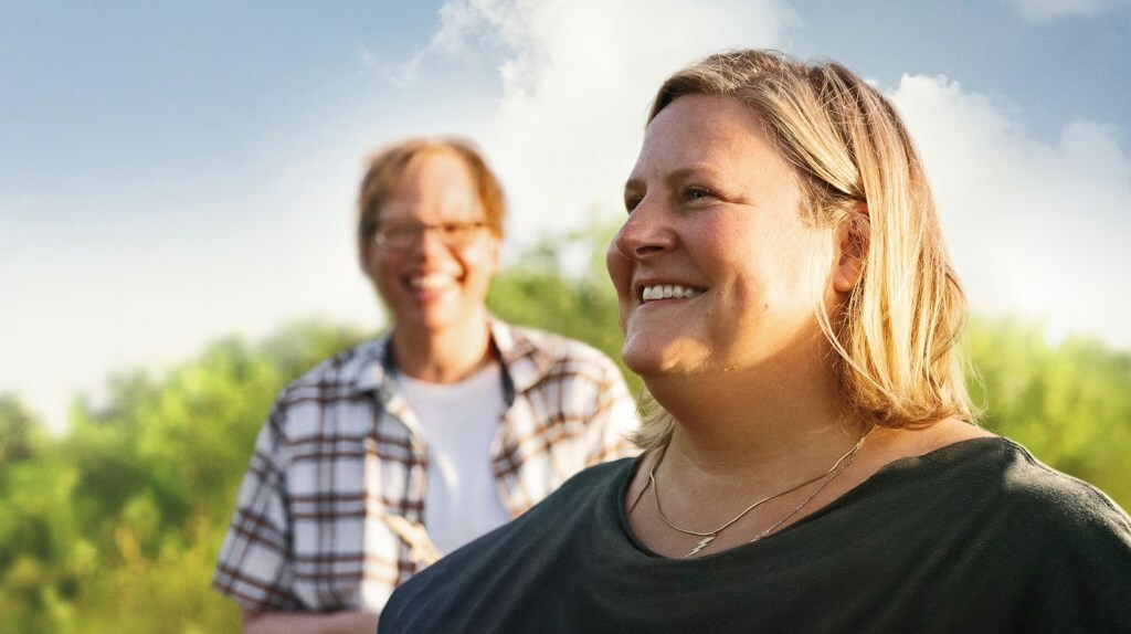 Jeff Hiller and Bridget Everett smile in a field in a still from 'Somebody Somewhere'.