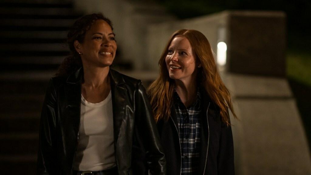 Tawny Cypress and Lauren Ambrose smile and walk down a sidewalk together at night in a still from 'Yellowjackets'.