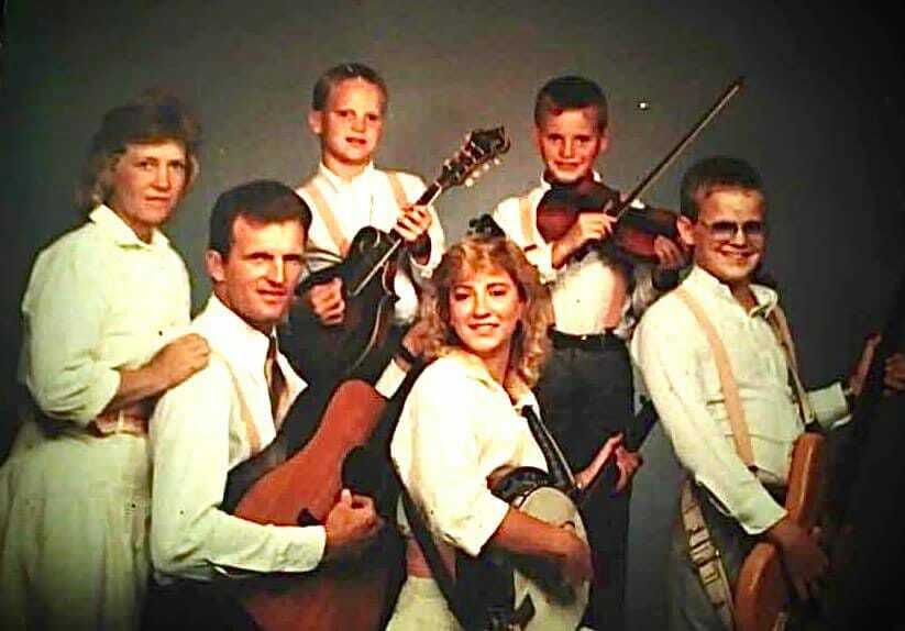 A vintage family portrait of The King’s Kidds, a gospel bluegrass group. The family members, dressed in coordinated white outfits, hold their instruments — guitars, mandolin, fiddle, banjo, and bass — posing for a professional photo. Their expressions convey unity, faith, and a deep connection to their music and ministry.