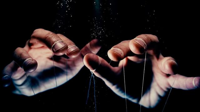 Auf dem Bild sind Hände zu sehen, die im Dunklen an Fäden ziehen. Auf dem Bild sind Hände zu sehen, die im Dunklen an Fäden ziehen.