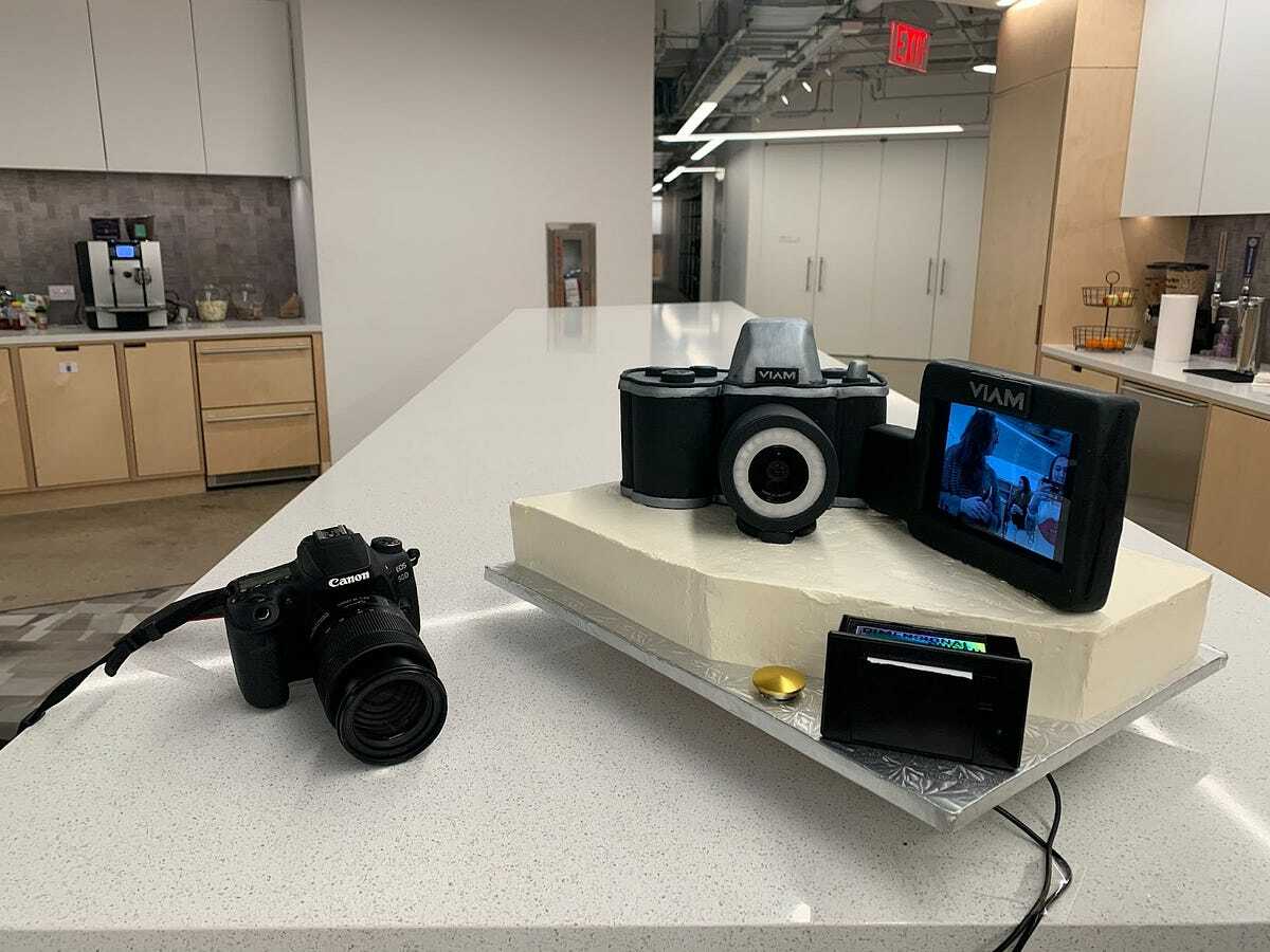 A photo of a canon camera, next to the interactive cake that has a camera on it as well as a display, button and a thermal printer