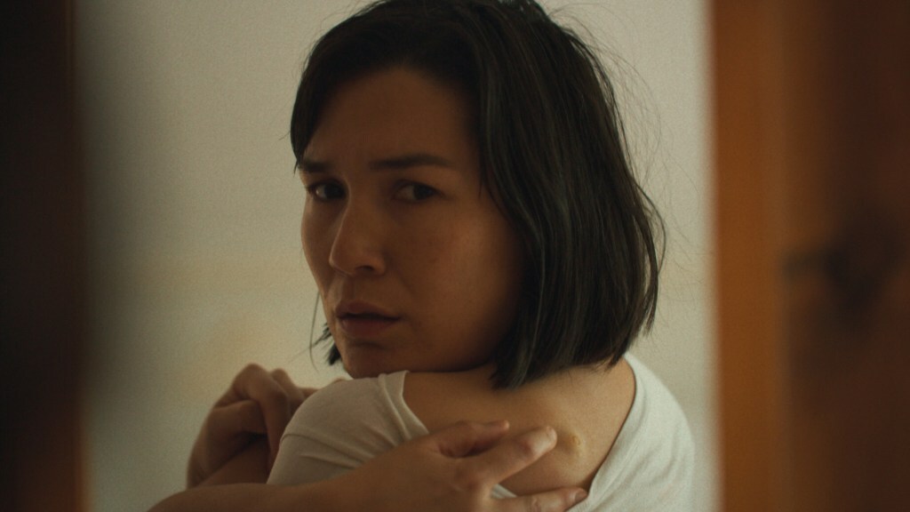 Zoë Chao looks over her shoulder into a mirror at a tick bite on her back in a still from 'The True Beauty of Being Bitten by a Tick'. Zoë Chao looks over her shoulder into a mirror at a tick bite on her back in a still from 'The True Beauty of Being Bitten by a Tick'.