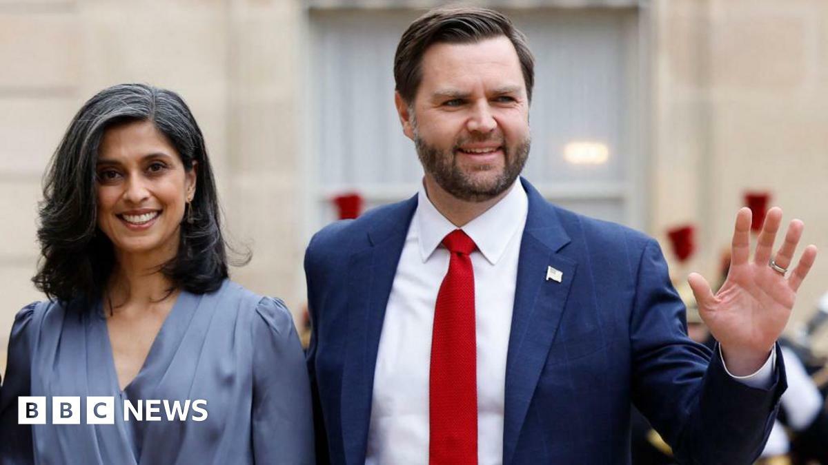 Usha Vance wears a blue dress and smiles. She stands next to JD Vance, who is wearing a suit and waving.