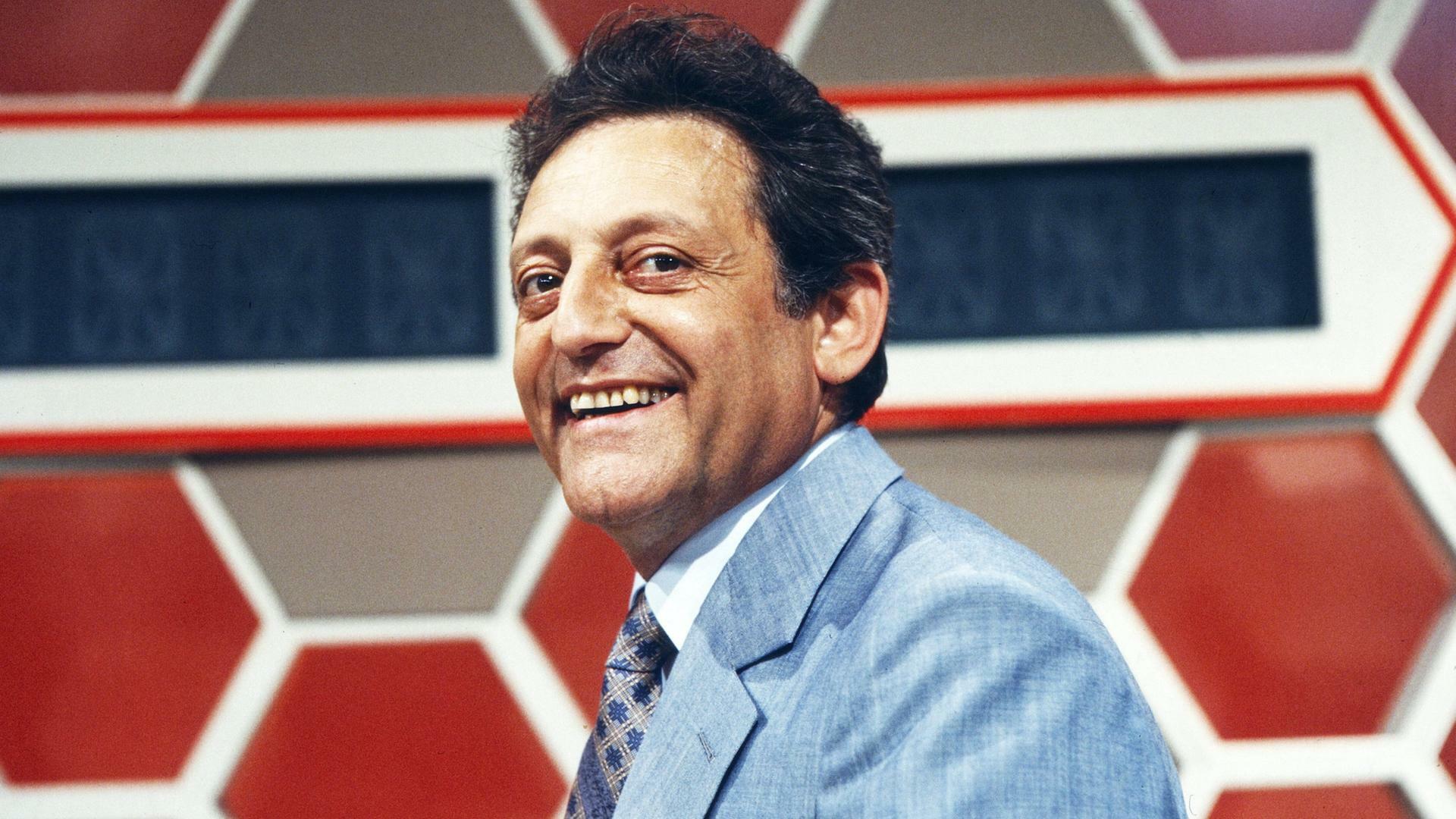 Hans Rosenthal steht vor dem typischen Waben-Hintergrund im Studio seiner Sendung "Dalli Dalli" und lacht in die Kamera