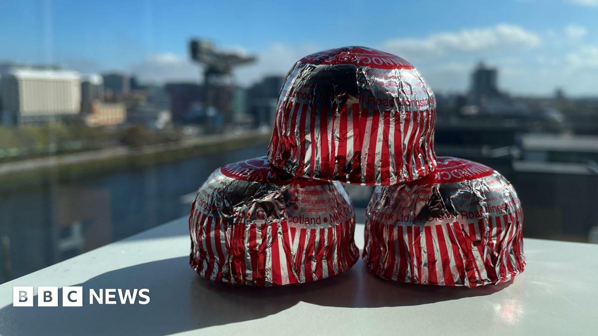 Three Tunnock's teacakes stacked up on a table. The Clyde and the Finnieston Crane can be seen through a window behind.