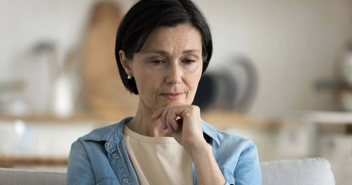 Eine Frau im mittleren Alter blickt nachdenklich auf einen Laptop-Bildschirm.