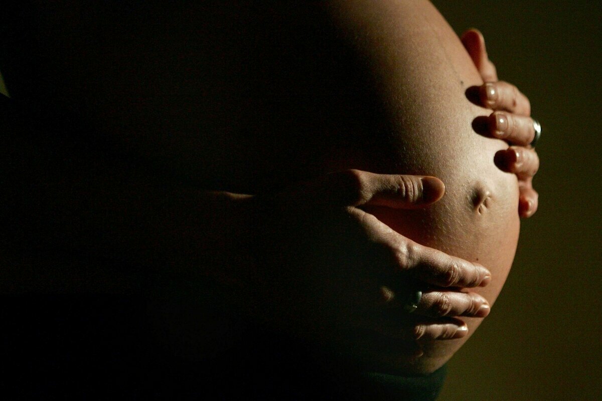 Eine hochschwangere Frau fasst sich mit beiden Händen an ihren Bauch