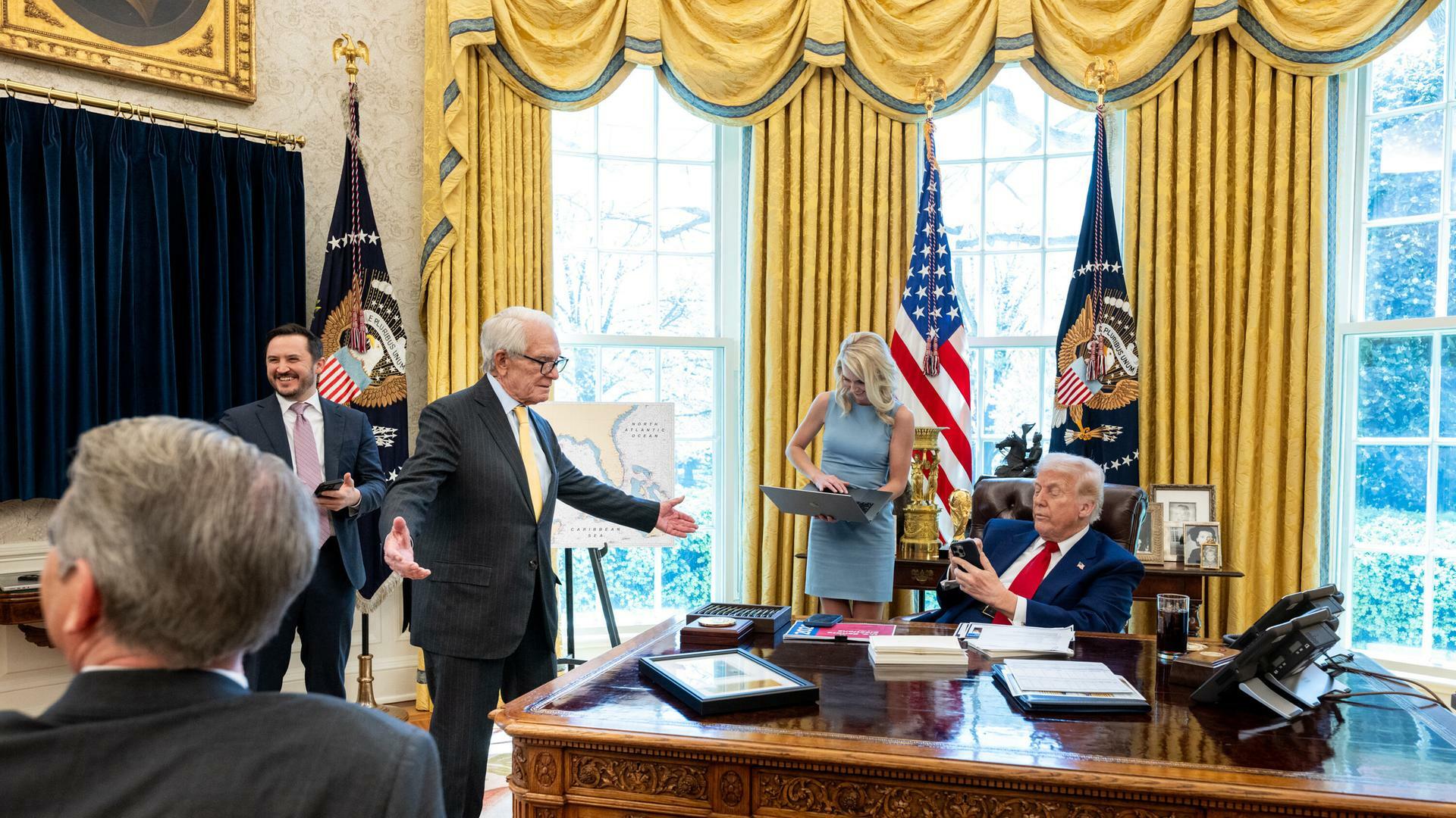 US-Präsident Donald Trump sitzt an seinem Arbeitsplatz im Oval Offices und trifft sich mit dem Milliardär Charles Schwab. Anwesend sind noch weitere Geschäftsmänner und Trumps Assistentin. 