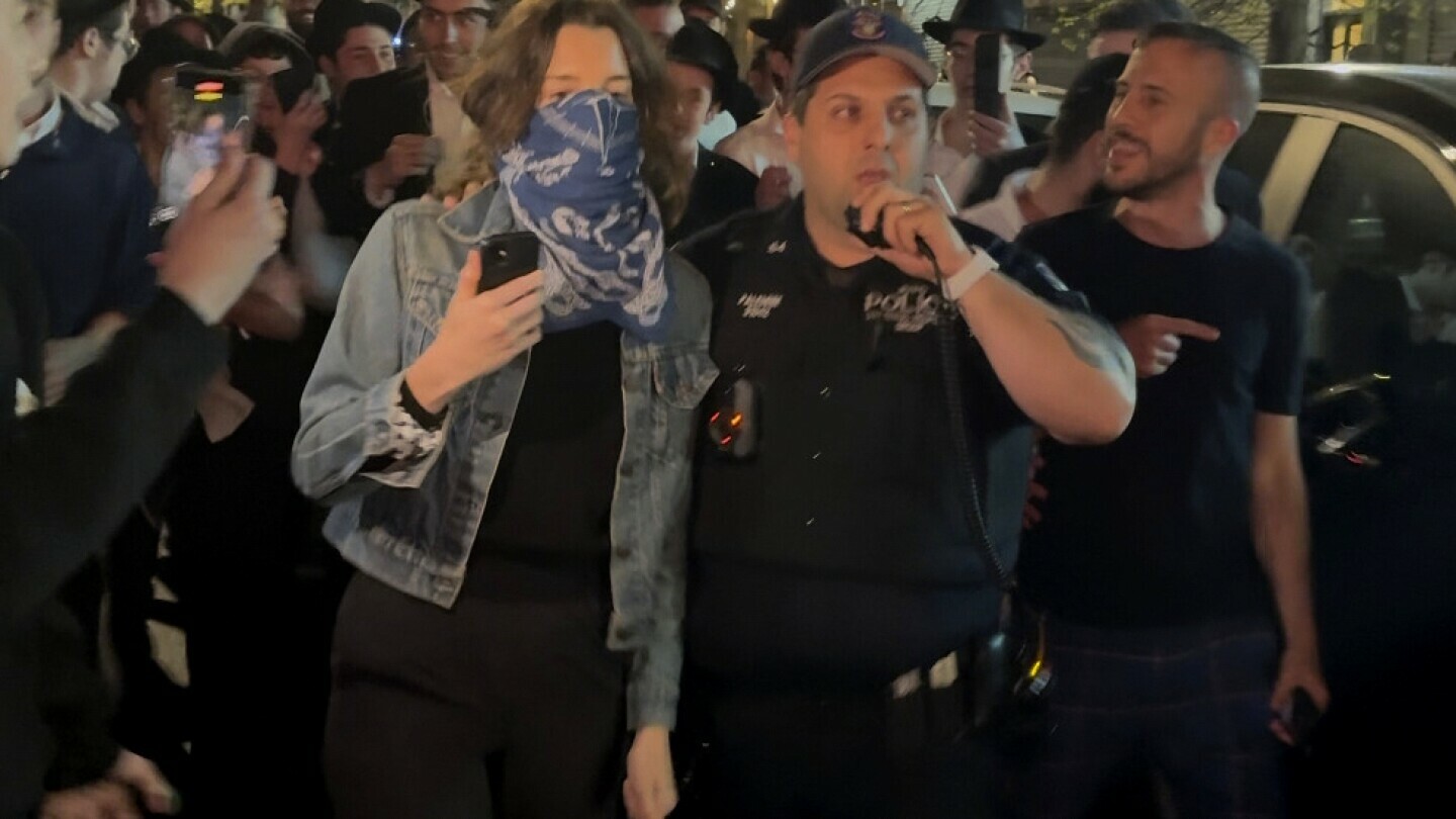This image taken from video shows a woman and a police officer as they are pursued by a mob of Orthodox Jewish men in the Crown Heights section of Brooklyn, N.Y., on Thursday, April 24, 2025. (AP Photo)
