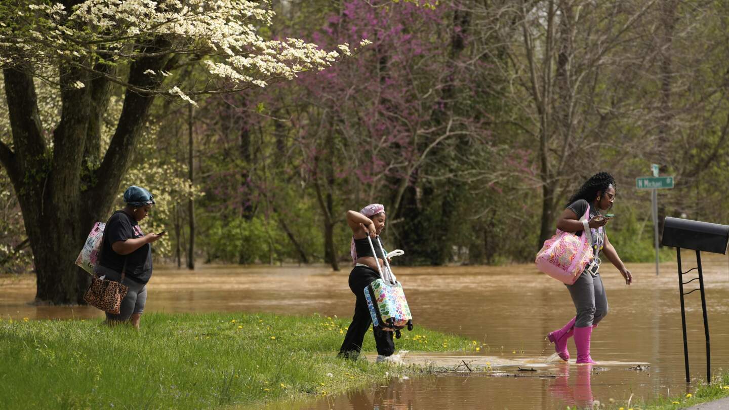 Marquetta Wheeler, right, with Samaria Williams and Jemaria Shaw, walk through flood waters as they leave their home on Marietta Drive in Hopkinsville, Ky., April 4, 2025. (AP Photo/George Walker IV, File)