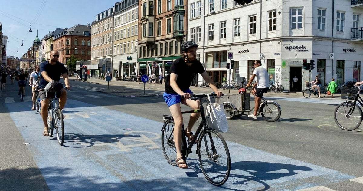 Radfahrerinnen und Radfahrer überqueren eine Kreuzung. Einer trägt einen Helm, die übrigen nicht.