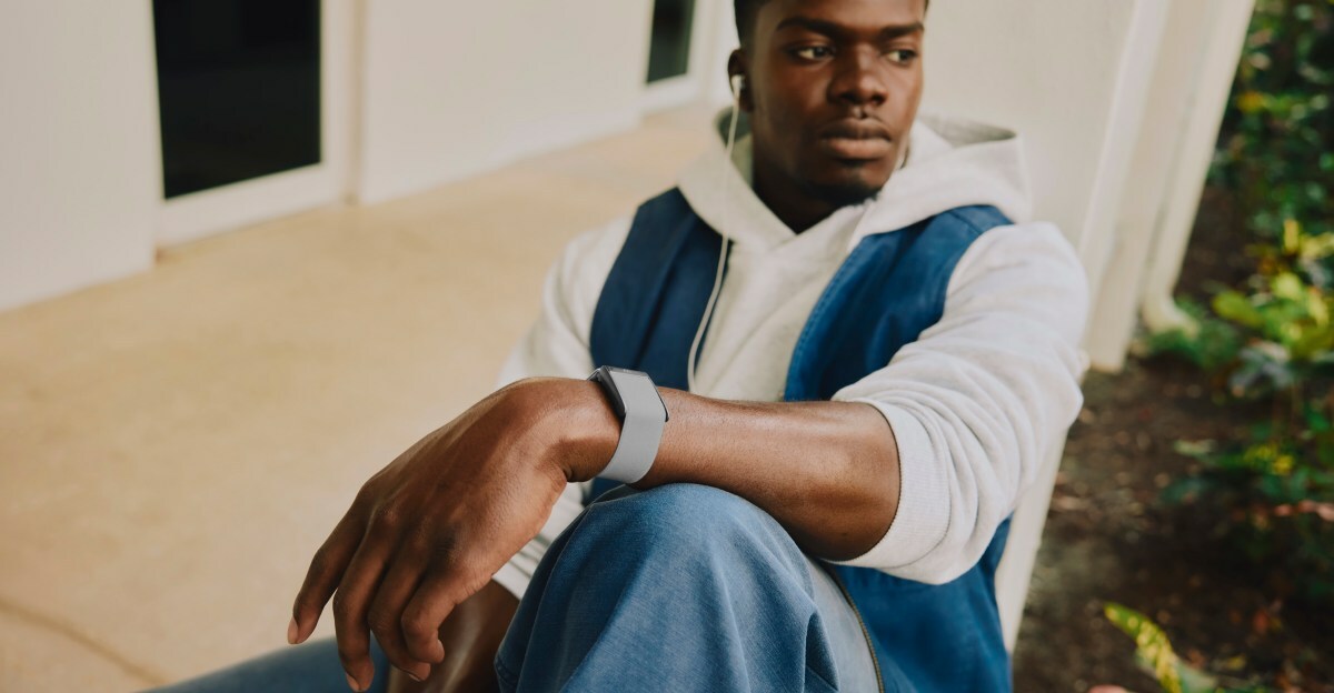 A lifestyle image of a young man wearing a light blue colored Whoop 5.0 band while casually relaxing on a front porch.
