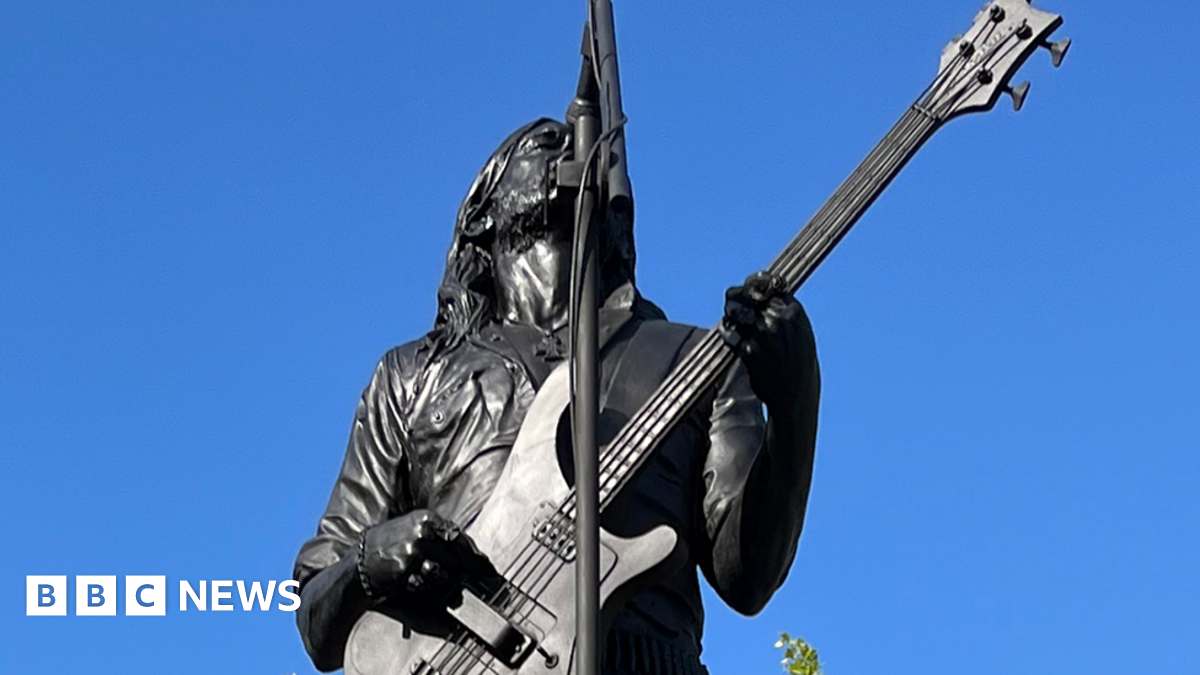 A black-coloured statue of Lemmy holding a bass guitar and singing up towards a microphone