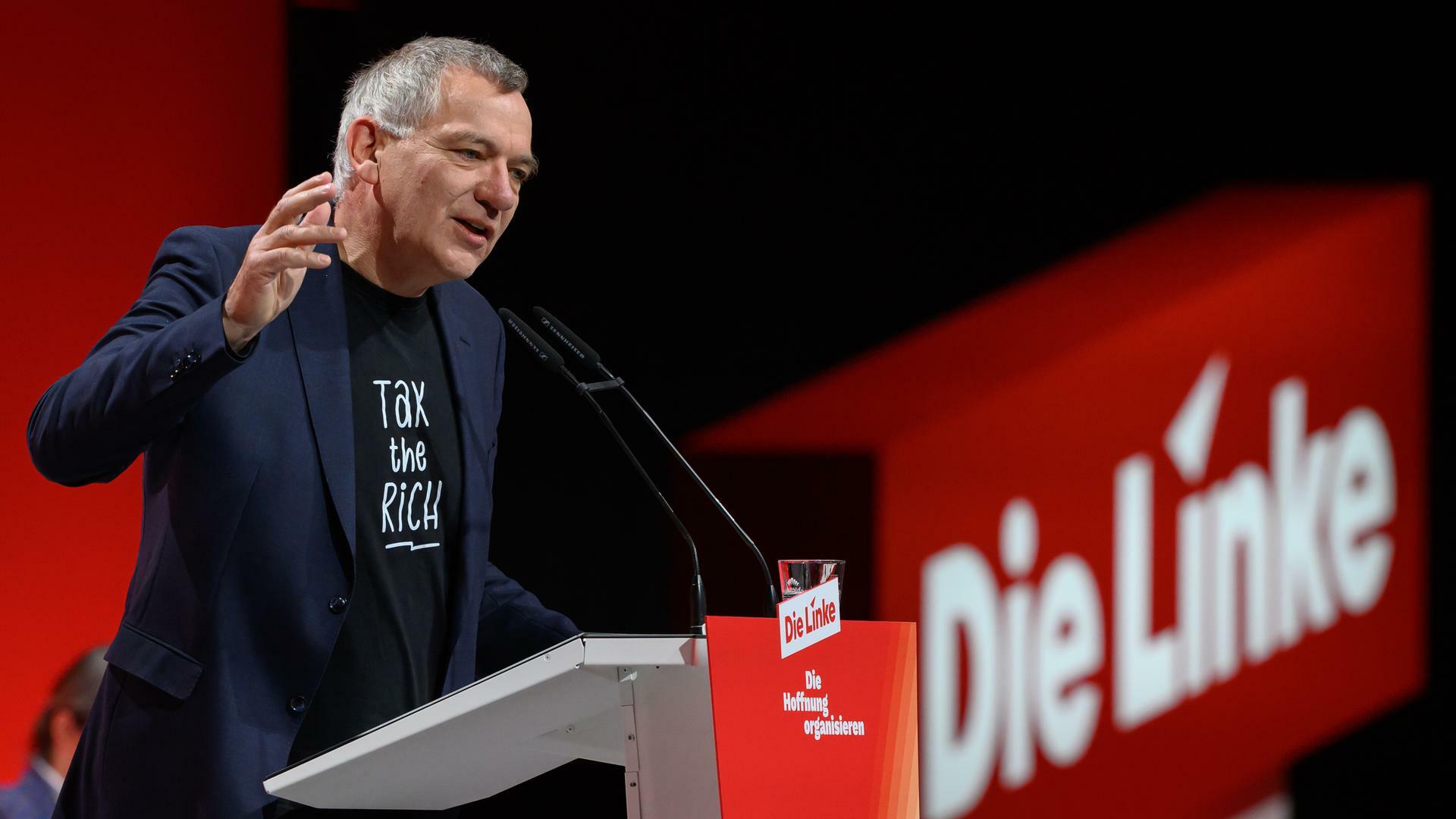 Jan van Aken steht am Rednerpult und gestikuliert mit der rechten Hand. 