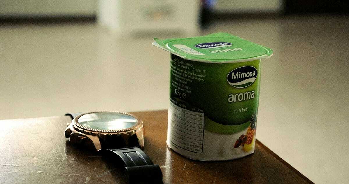 A single serve cup of yogurt next to a wristwatch.