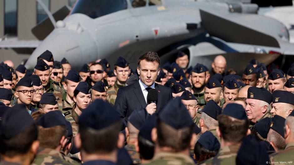 French President Emmanuel Macron stands amid French airforce personnel with a Dassault Rafale fighter jet behind him on 18 March 2025.