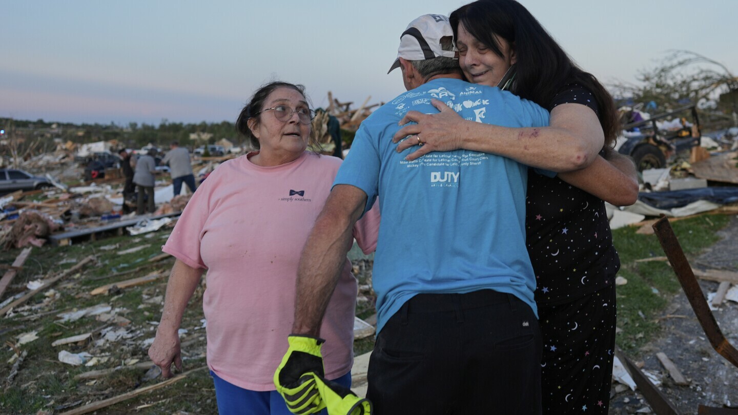 Bea Johnson, left, looks to her sister Kristie Sexton, right, as she is embraced by family friend Keith Adams as they stand next to Sexton's destroyed home after a severe storm passed through the area, Saturday, May 17, 2025, in London, Ky. (AP Photo/Carolyn Kaster)