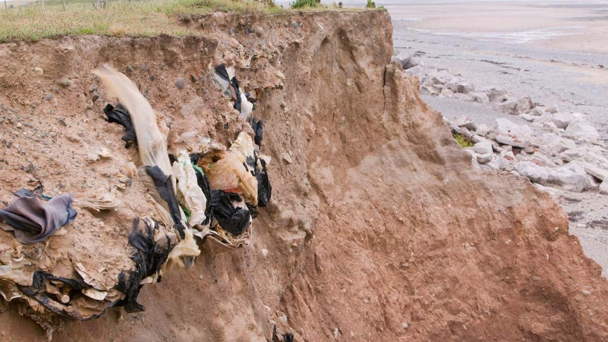 Old landfill rubbish revealed in sea cliffs by coastal erosion on Walney Island, UK. | Global Warming Images/Alamy