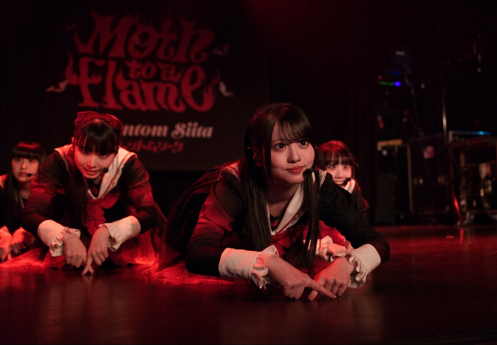 The photo depicts a moment in Phantom Siita's performance during their show in London. The five members are on stage, dressed in the same costums and kneeling on the ground while leaning forward and placing the pointing fingers on the ground. Photography by JJ Grant (Wonderlens)