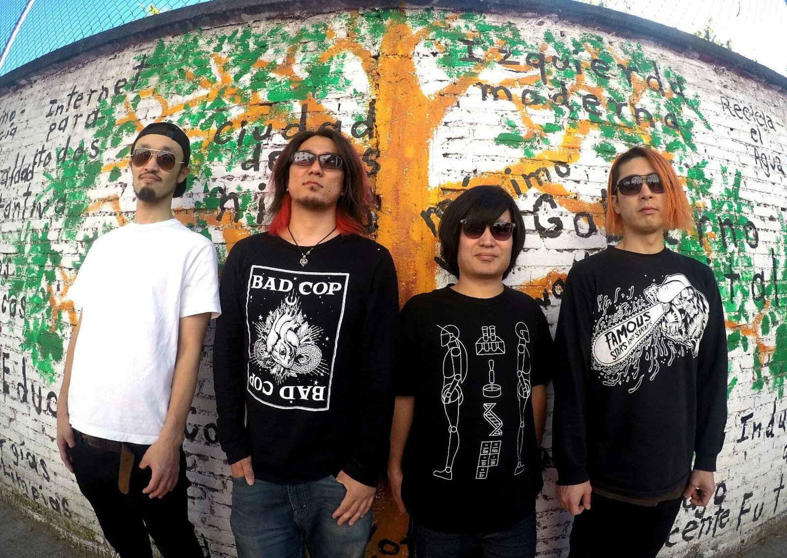 The photo shows the four members of STONE LEEK standing in front of a wall covered with graffiti. The graffiti includes a tree with green leaves and (Spanish) words. Three of the members wear black (sweat) shirts and one wears a white shirt.