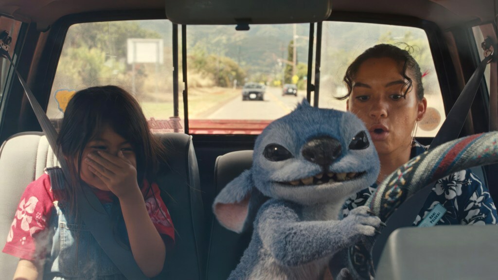 Maia Kealoha and Sydney Agudong ride in a truck as blue alien Stitch grabs the wheel in a still from 'Lilo & Stitch'.