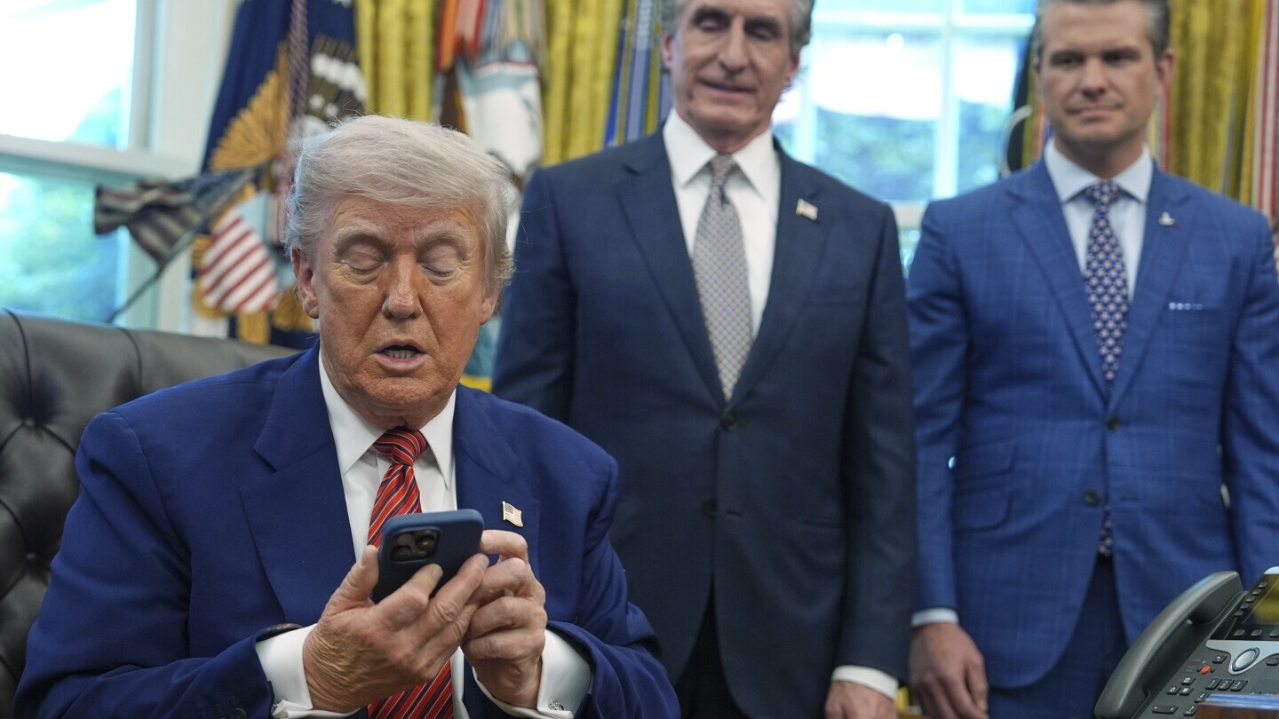 President Donald Trump silences his phone that rang twice as he was speaking to reporters after signing executive orders regarding nuclear energy in the Oval Office of the White House, Friday, May 23, 2025, in Washington, as Interior Secretary Doug Burgum and Defense Secretary Pete Hegseth watch. (AP Photo/Evan Vucci)