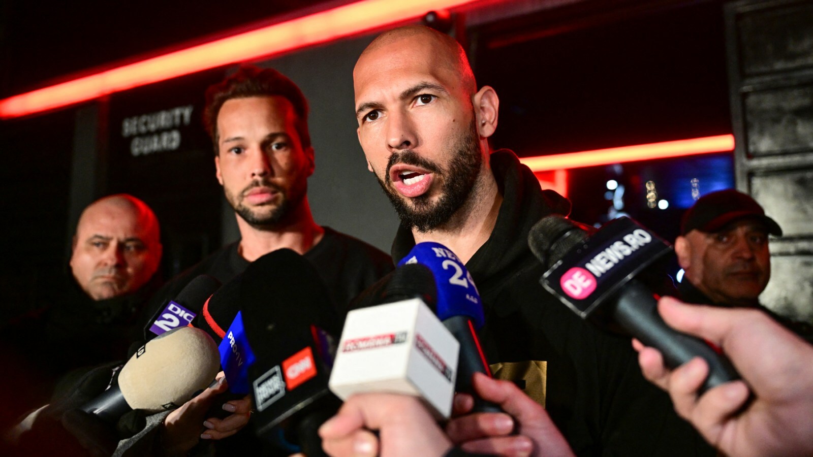 Andrew Tate (R) and his brother Tristan (2R) speak to the media as they arrive in Romania back from US, in Bucharest March 22, 2025. Self-described misogynist influencer Andrew Tate return to Romania, where he is facing rape and human trafficking charges, after a trip to the US. The British-American figurehead of the online masculinist movement travelled to Florida, together with his brother, last month, marking the first time he had been out of the eastern European country since his 2022 arrest. Under judicial supervision, the Tates need to report to authorities on March 24, a no-show potentially leading to "preventive arrest", according to Romanian authorities. (Photo by Daniel MIHAILESCU / AFP) (Photo by DANIEL MIHAILESCU/AFP via Getty Images)