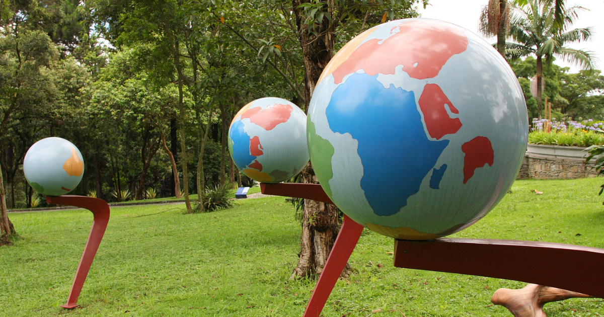 Três globos terrestres suspensos numa estrutura em um parque com gramado e árvores