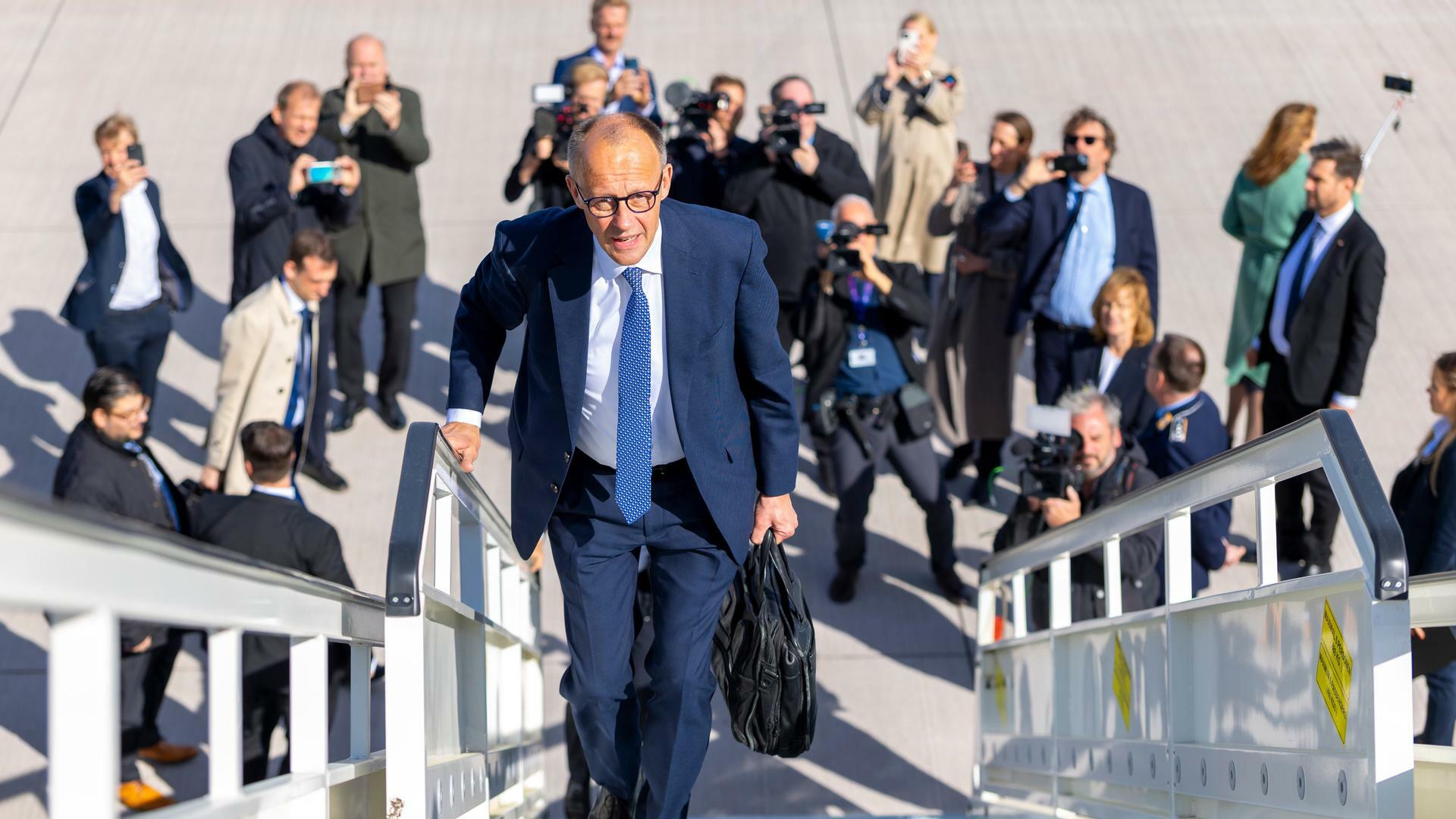 Friedrich Merz läuft die Gangway eines Fliegers hinauf. Unter ihm am Boden stehen Fotografen und fotografieren zu ihm hinauf. Friedrich Merz läuft die Gangway eines Fliegers hinauf. Unter ihm am Boden stehen Fotografen und fotografieren zu ihm hinauf.