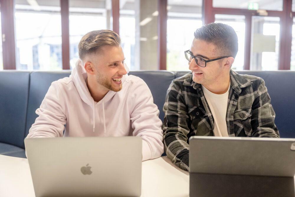 Zwei Studierende sitzen an ihren Laptops nebeneinander.