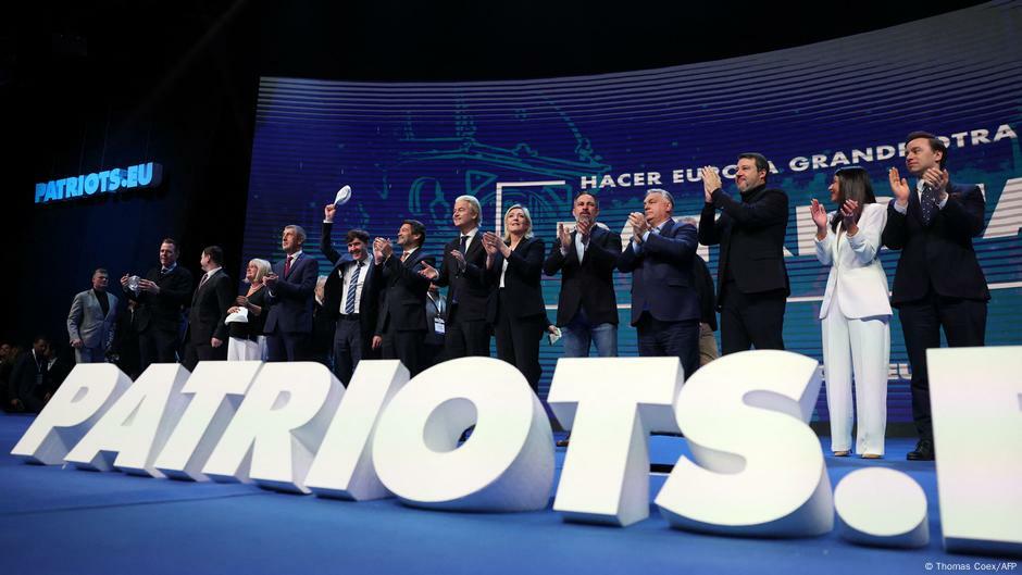 Men and women clap as they stand on a stage in front of a blue backdrop with Spanish words and behind the word 'Patriots' spelled out in large white letters. Madrid, Spain, 8 February 2025. | Image: Thomas Coex/AFP