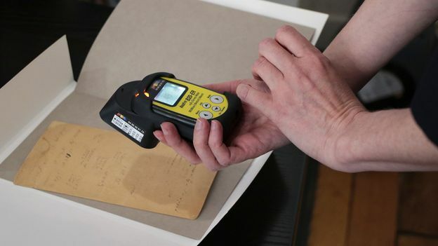 A person holds a Geiger counter up to an antique document. | Credit: Taufenbach and Bastien Pourtout