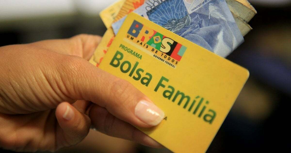 Nahaufnahme einer Hand, die mehrere brasilianische Geldscheine hält sowie eine gelbe Scheckkarte mit dem Aufdruck „Programa Bolsa Familia“