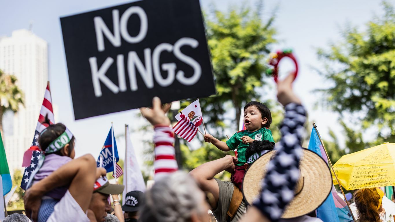 A black sign reading No Kings in white text in front of a little kid on someone's shoulders.