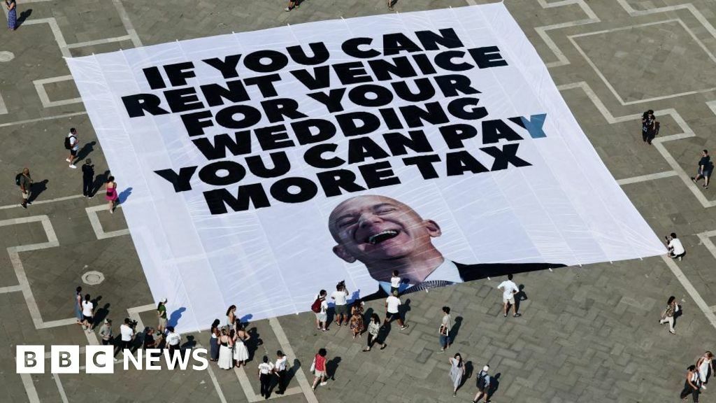A large banner against Amazon founder Jeff Bezos lies on the ground, placed by Greenpeace Italy activists and UK activist group Everyone Hates Elon, on the ground of St Mark's Square, on 23 June, 2025. It is white with black lettering in capitals and has a picture of Bezos throwing his head back laughing
