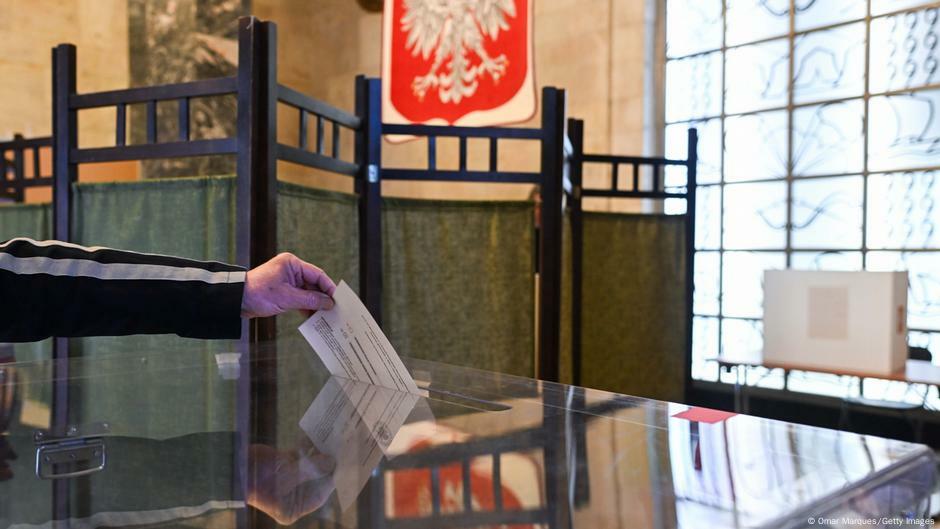 A hand drops a ballot into a ballot box. The Polish coat of arms is reflected in the surface of the ballot box. | Image: Omar Marques/Getty Images