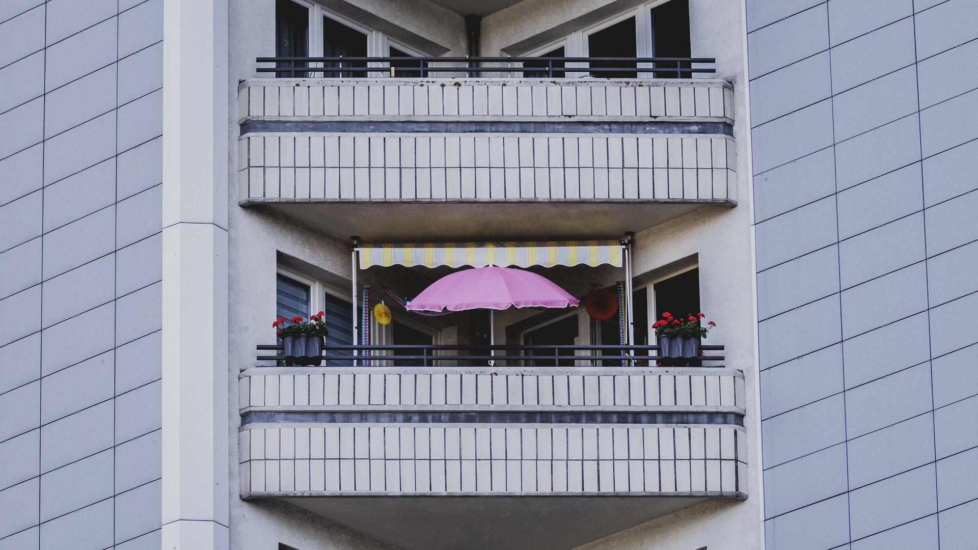 Das Foto zeigt einen pinkfarbenen Sonnenschirm auf dem Balkon eines Plattenbaus mit grauer Fassade in Berlin.