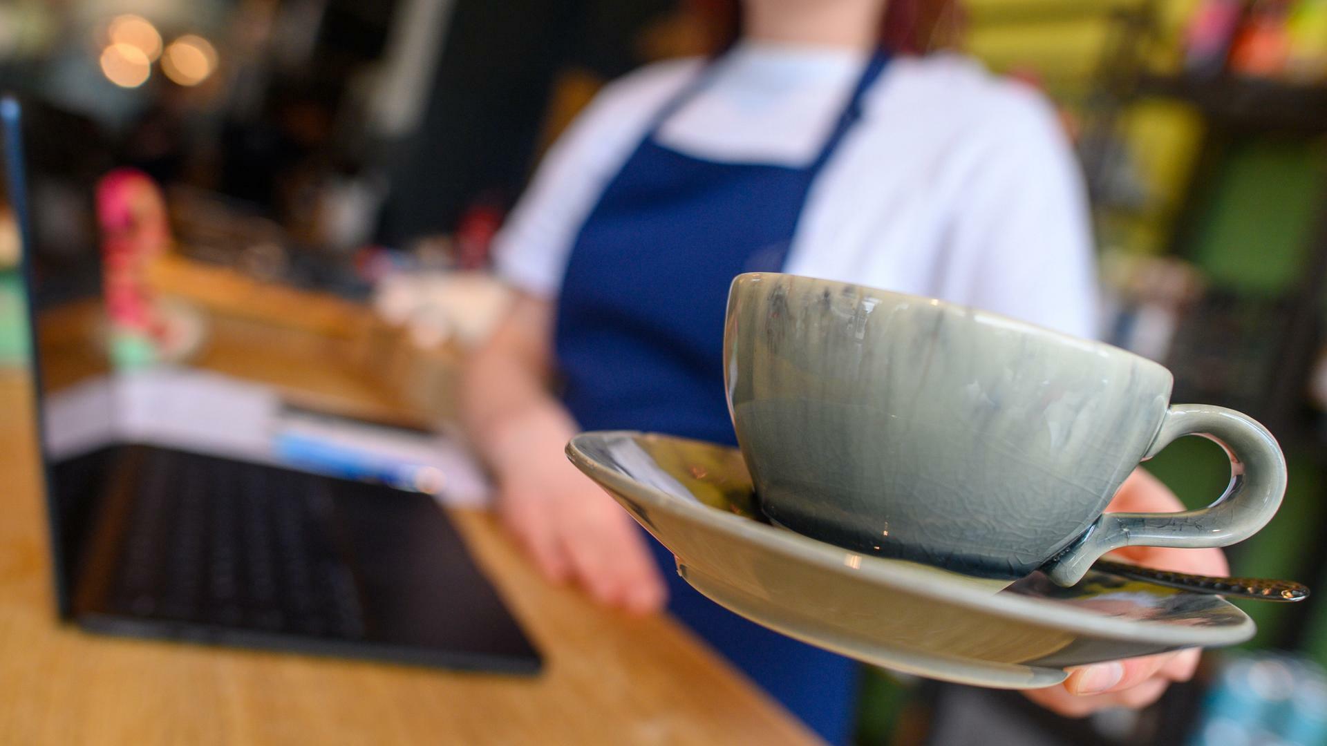 Eine Bedienung bringt in einem Café eine Tasse an einen Tisch.