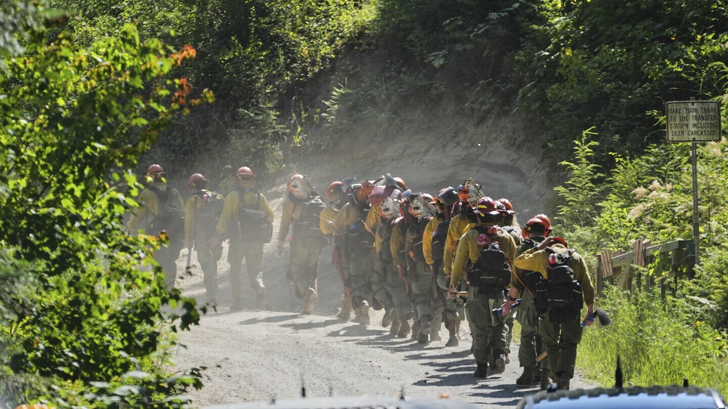 A line of wildland firefighters arrive at the scene the day after a shooter ambushed and killed multiple firefighters responding to a wildfire at Canfield Mountain Monday, June 30, 2025, in Coeur D'Alene, Idaho. (AP Photo/Lindsey Wasson)
