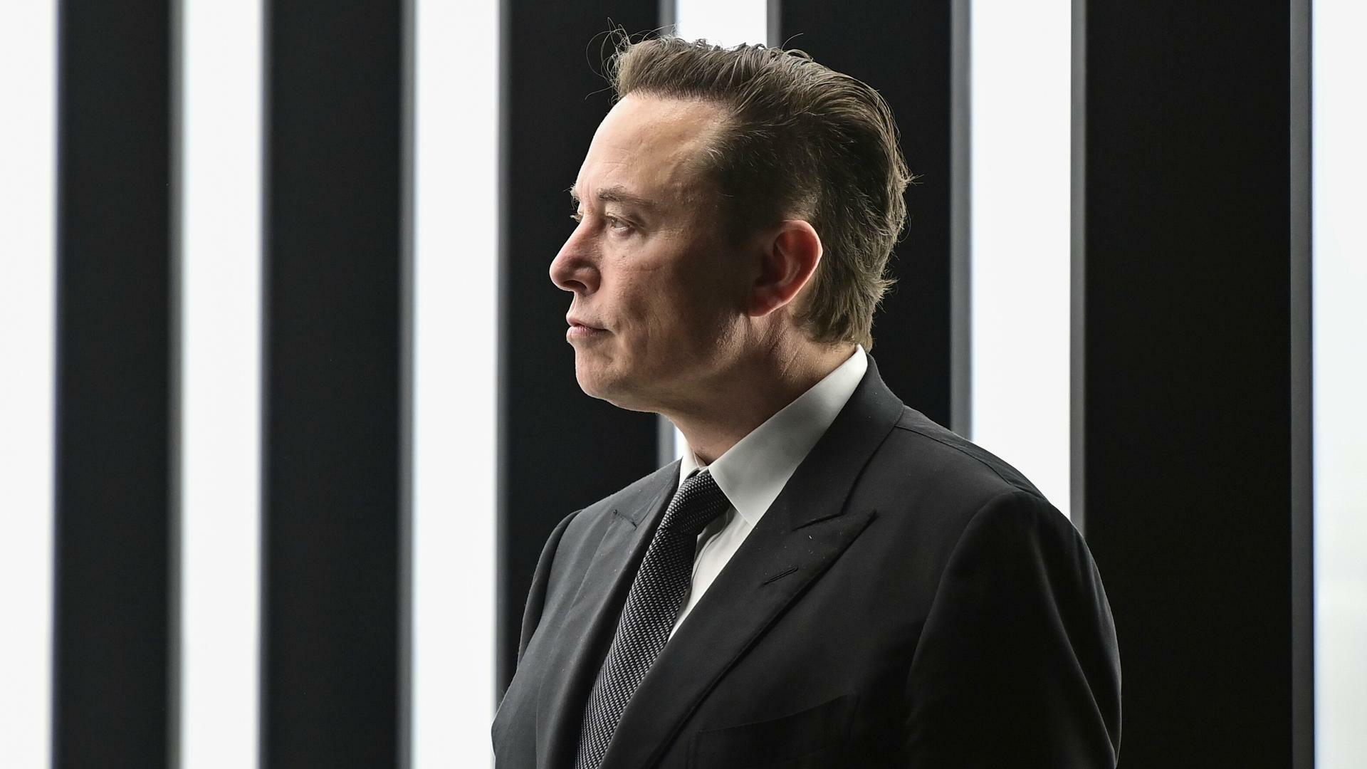 Tech-Milliardär Elon Musk im schwarzen Anzug vor schwarz-weißem Hintergrund. 